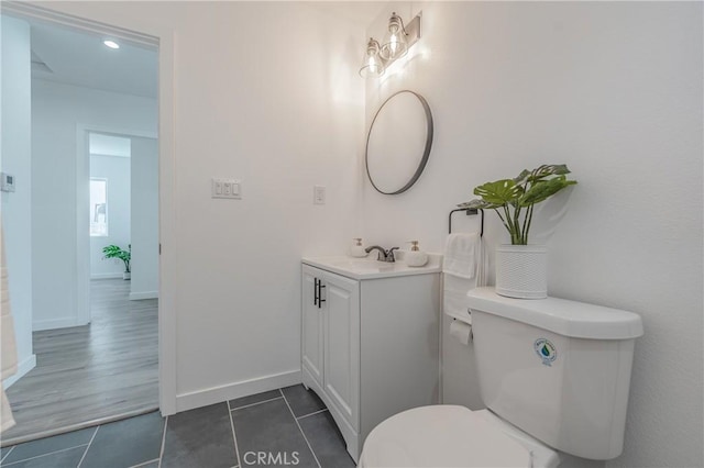 half bath featuring tile patterned floors, baseboards, toilet, and vanity