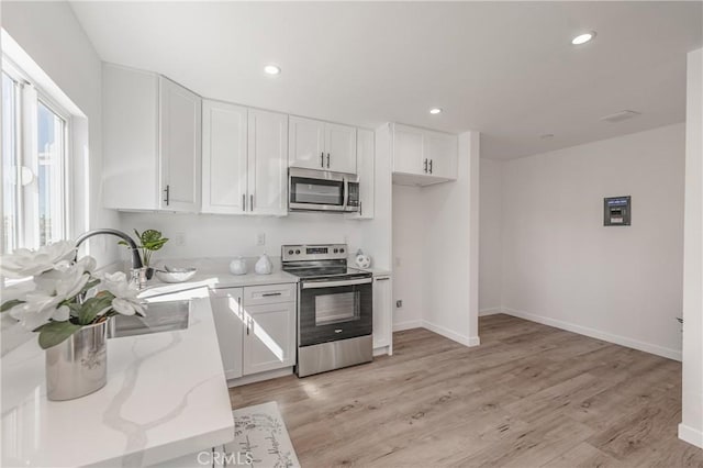 kitchen featuring light stone countertops, recessed lighting, appliances with stainless steel finishes, light wood-style floors, and white cabinets