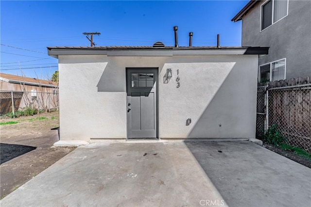 view of exterior entry with stucco siding, a patio area, and fence