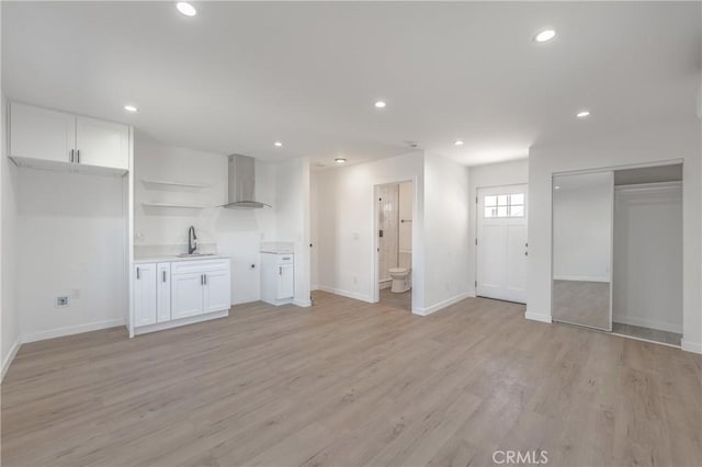 kitchen featuring a sink, light wood-type flooring, white cabinetry, and wall chimney range hood