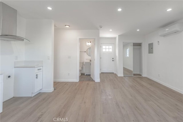 unfurnished living room featuring a wall unit AC, baseboards, light wood-style flooring, electric panel, and recessed lighting