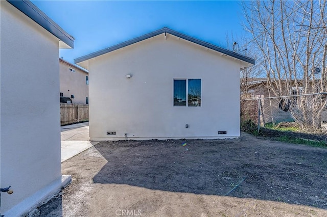 view of side of home with crawl space, stucco siding, and fence