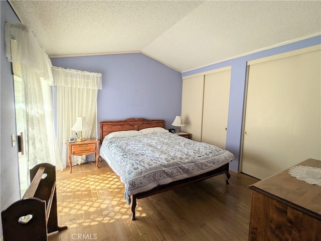 bedroom featuring a textured ceiling, multiple closets, hardwood / wood-style flooring, and vaulted ceiling