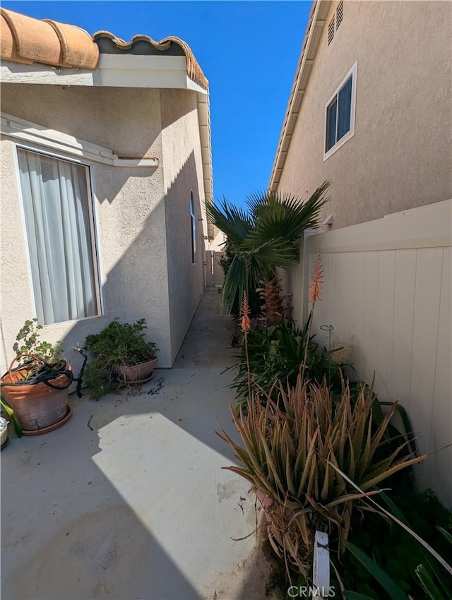 view of side of property featuring stucco siding, a patio, and fence