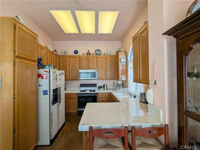 kitchen featuring tile countertops, a sink, white fridge with ice dispenser, range with gas cooktop, and stainless steel microwave