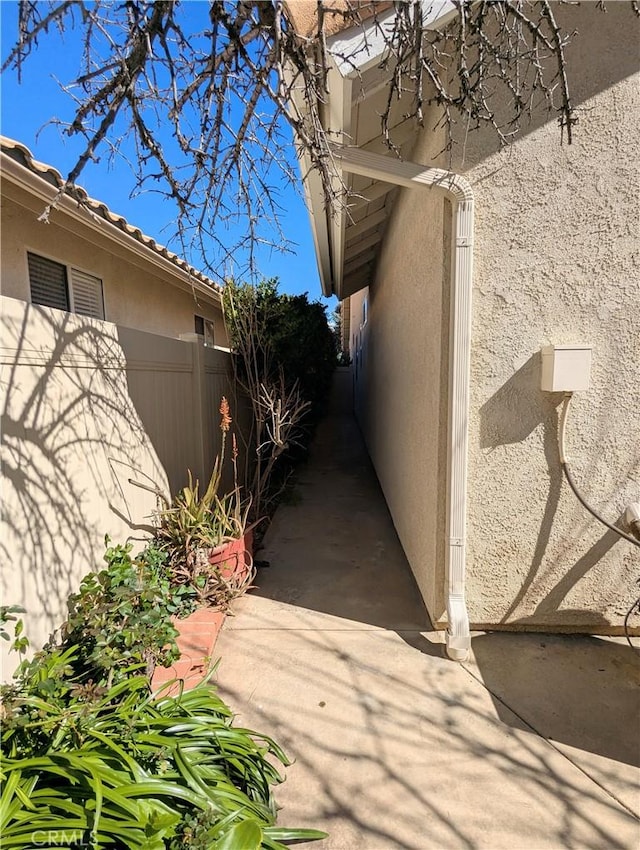 view of side of property featuring stucco siding, a tiled roof, and fence