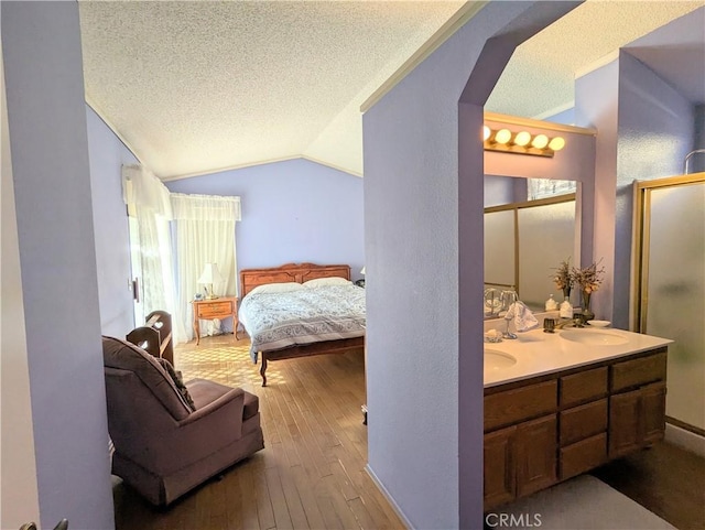 bedroom featuring a sink, a textured ceiling, arched walkways, wood-type flooring, and vaulted ceiling