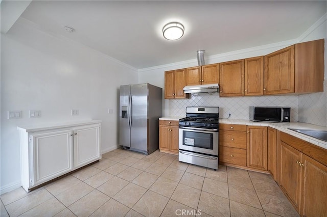 kitchen with brown cabinetry, light countertops, under cabinet range hood, appliances with stainless steel finishes, and tasteful backsplash