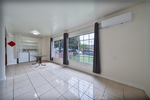 tiled spare room with baseboards, an AC wall unit, and washing machine and dryer