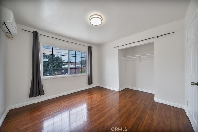 unfurnished bedroom featuring wood finished floors, baseboards, an AC wall unit, a closet, and a barn door