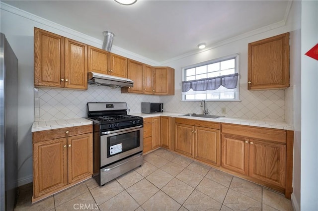 kitchen with backsplash, crown molding, under cabinet range hood, appliances with stainless steel finishes, and a sink