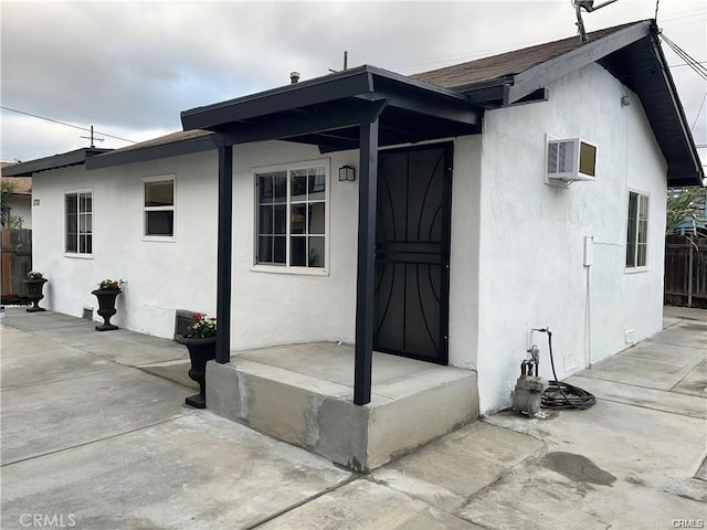 exterior space with a patio area, stucco siding, a wall mounted AC, and fence