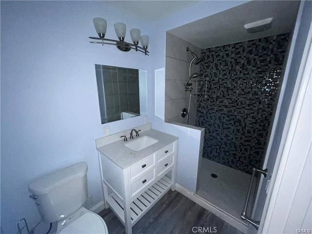 bathroom featuring tiled shower, toilet, vanity, and wood finished floors