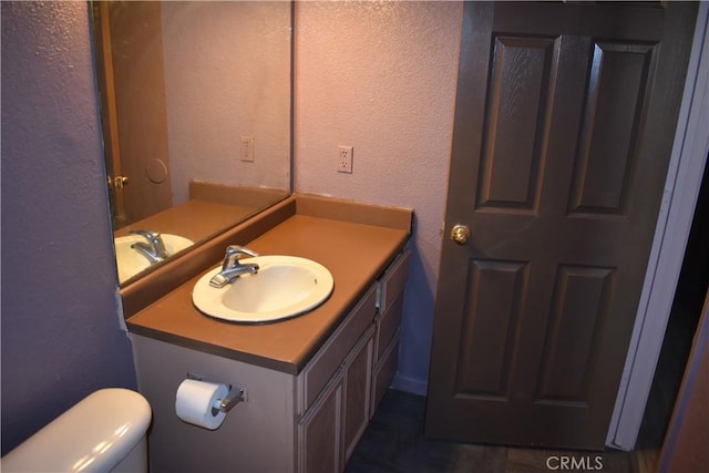 half bathroom with toilet, vanity, and a textured wall