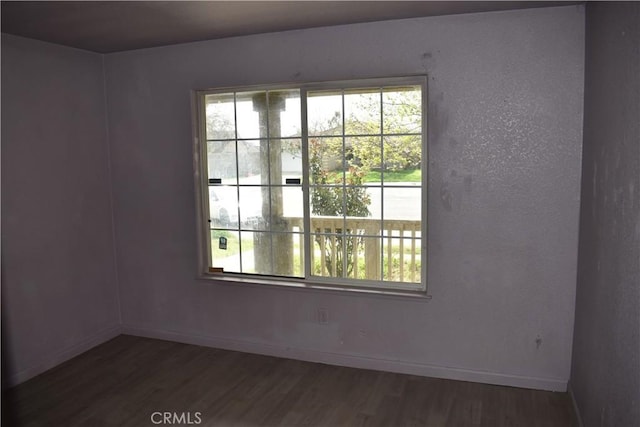 unfurnished room with baseboards, dark wood-type flooring, and a healthy amount of sunlight