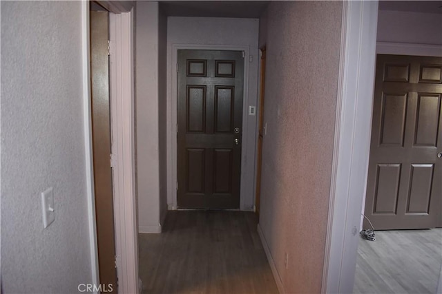 hall featuring wood finished floors, baseboards, and a textured wall