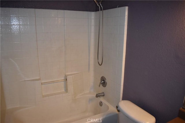 full bath featuring bathing tub / shower combination, toilet, and a textured wall