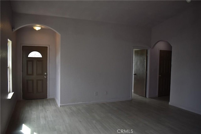 foyer entrance featuring light wood-style flooring, baseboards, and arched walkways