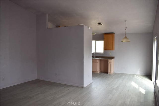 interior space featuring light wood-type flooring, visible vents, brown cabinets, and pendant lighting