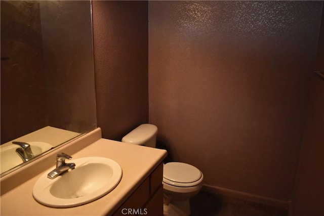 half bath with toilet, vanity, baseboards, and a textured wall