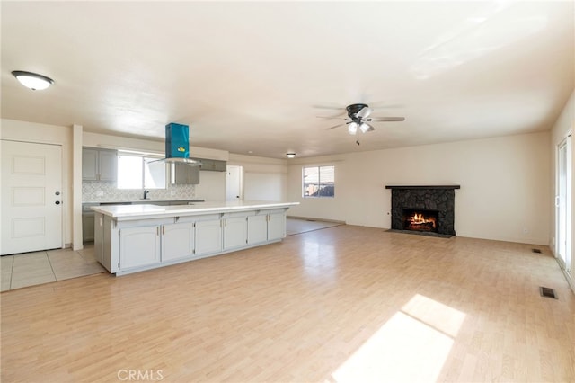 kitchen featuring backsplash, a fireplace with flush hearth, light countertops, island exhaust hood, and light wood-style floors