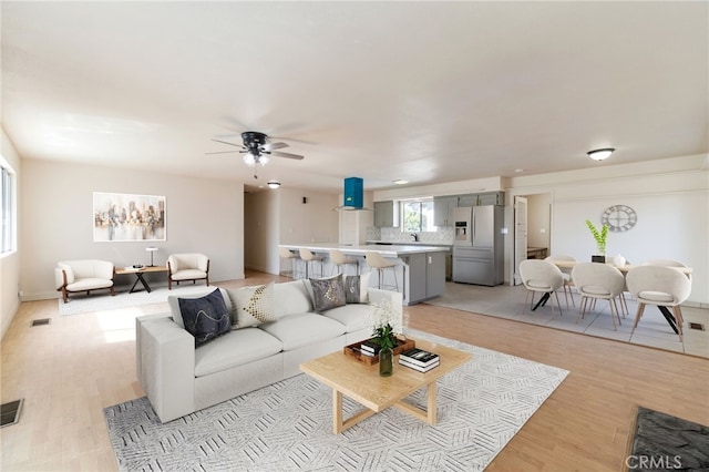 living room featuring visible vents, light wood-type flooring, and a ceiling fan