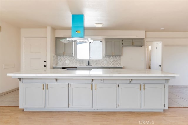 kitchen with light tile patterned floors, decorative backsplash, baseboards, and island range hood