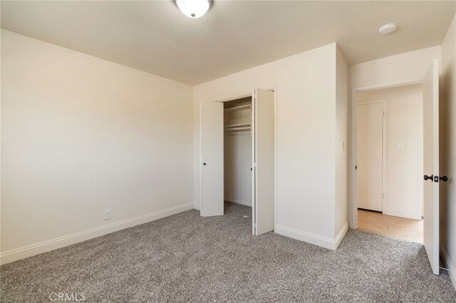 unfurnished bedroom with a closet, light colored carpet, and baseboards