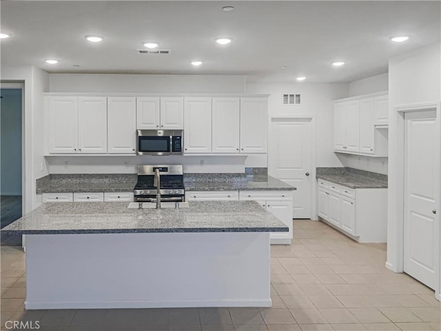 kitchen featuring a center island with sink, visible vents, dark stone counters, white cabinets, and appliances with stainless steel finishes