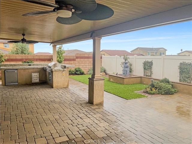 view of patio / terrace with area for grilling, a fenced backyard, a ceiling fan, and exterior kitchen