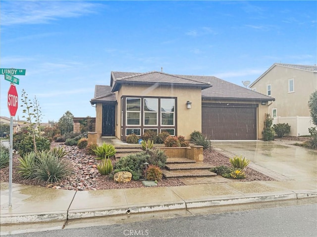 view of front of home with concrete driveway, an attached garage, fence, and stucco siding