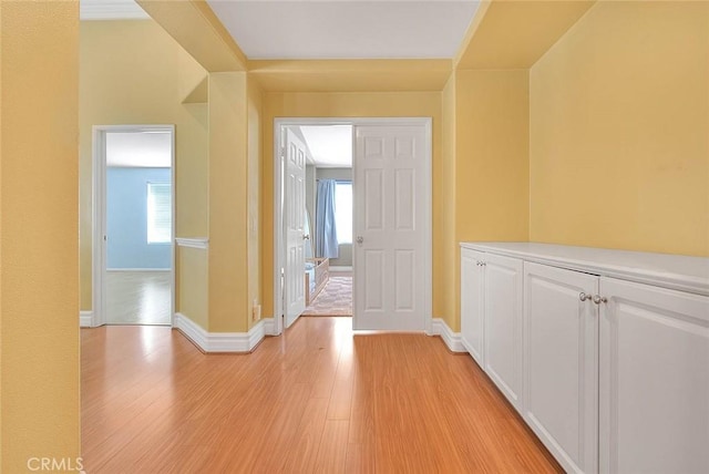 hall with baseboards, light wood-type flooring, and a wealth of natural light