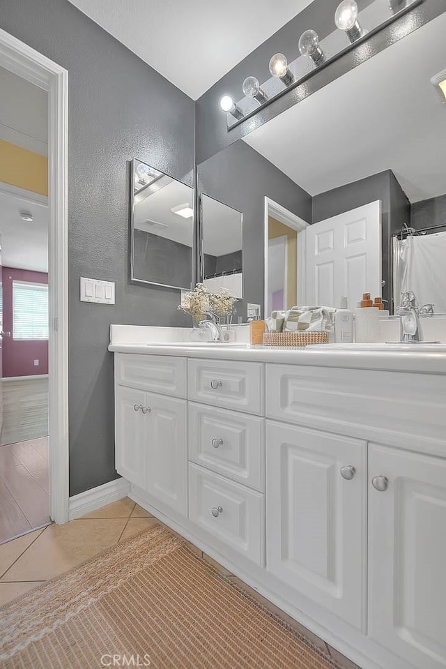 bathroom with tile patterned floors, double vanity, a textured wall, and a sink