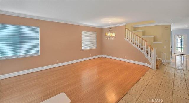 spare room featuring a notable chandelier, ornamental molding, light wood finished floors, baseboards, and stairs