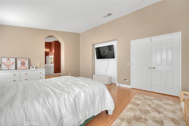 bedroom with light wood-style flooring, arched walkways, visible vents, and baseboards