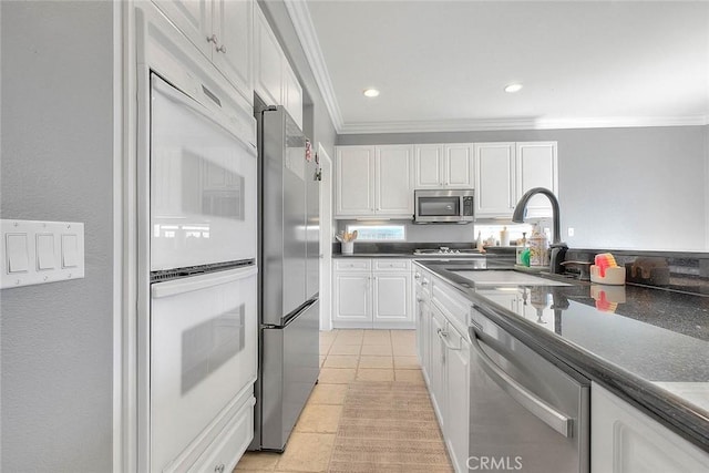 kitchen with a sink, dark countertops, white cabinetry, appliances with stainless steel finishes, and crown molding