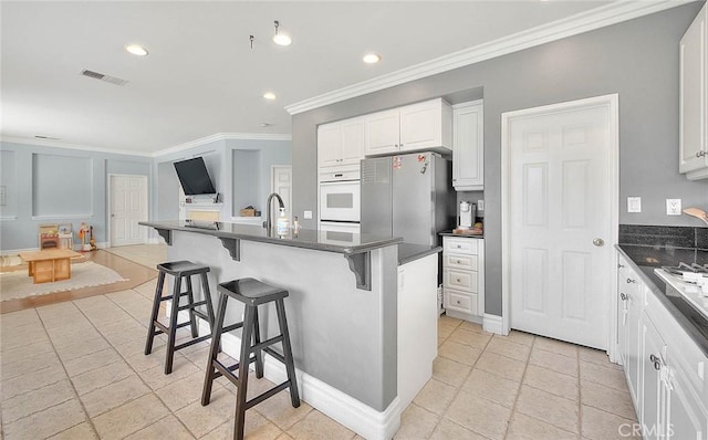 kitchen with dark countertops, a breakfast bar area, visible vents, and freestanding refrigerator