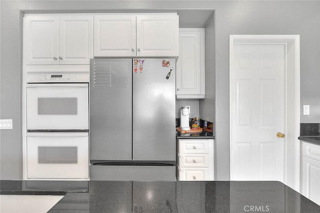 kitchen with white double oven, white cabinets, and freestanding refrigerator