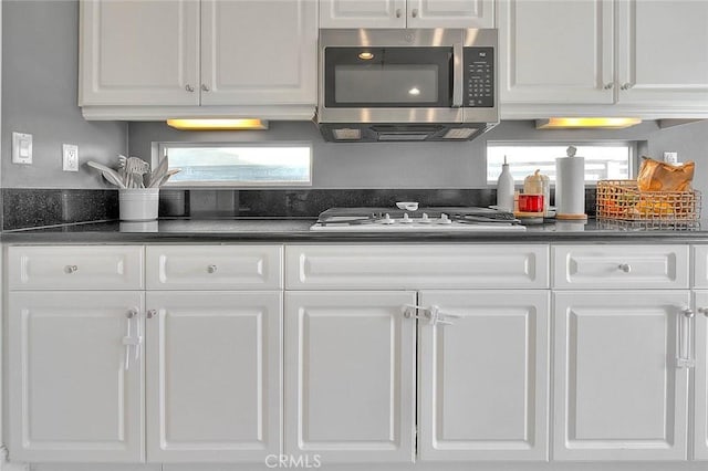 kitchen featuring stainless steel microwave, white cabinets, and dark countertops