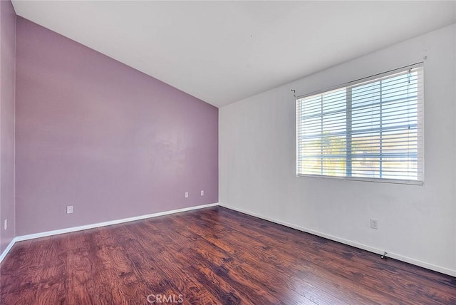 empty room with baseboards, dark wood-type flooring, and vaulted ceiling