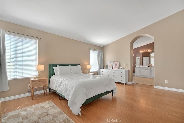 bedroom featuring arched walkways, multiple windows, lofted ceiling, and wood finished floors