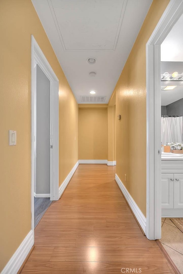 hallway featuring attic access, visible vents, light wood-type flooring, and baseboards