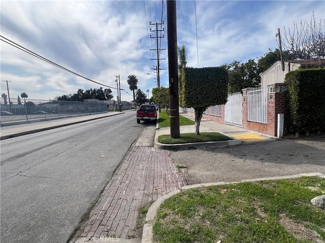 view of road featuring a gate, curbs, street lighting, and sidewalks