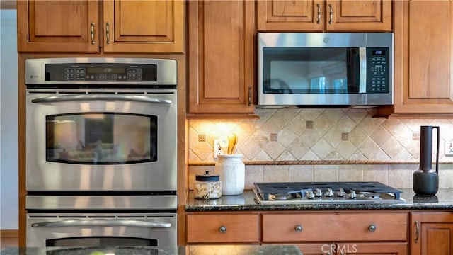 kitchen with dark stone countertops, brown cabinetry, backsplash, and stainless steel appliances