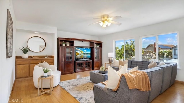 living area featuring baseboards, ceiling fan, and light wood finished floors