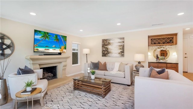 living area with recessed lighting, a fireplace with raised hearth, and ornamental molding