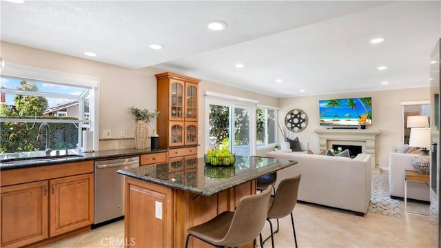 kitchen with a sink, a kitchen breakfast bar, stainless steel dishwasher, a center island, and a fireplace