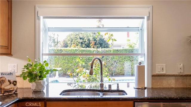 kitchen with a sink, dark stone counters, and brown cabinetry