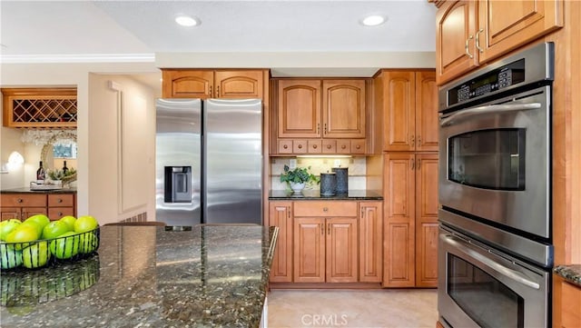 kitchen with recessed lighting, brown cabinets, appliances with stainless steel finishes, and dark stone counters