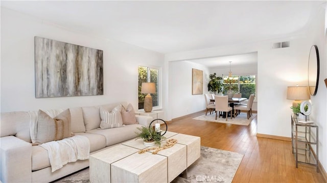 living area with a chandelier, visible vents, baseboards, and wood-type flooring